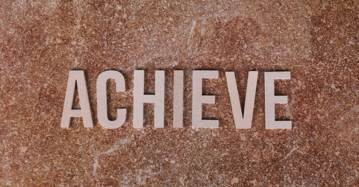 Wooden letters spelling 'ACHIEVE' on a textured brown surface, conveying motivation and success.